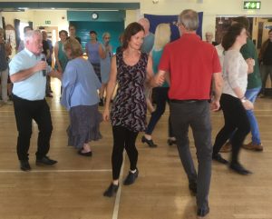 Four couples dancing, turning their partners with the left arm. Other people watching in the background.