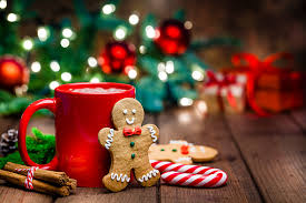 Gingerbread man next to a red mug with christmas tree and lights in background